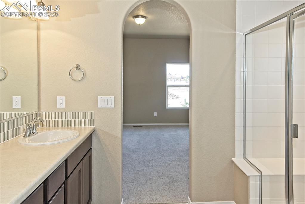 Image 18 of 25: Bathroom with vanity, tiled shower, and decorative backsplash