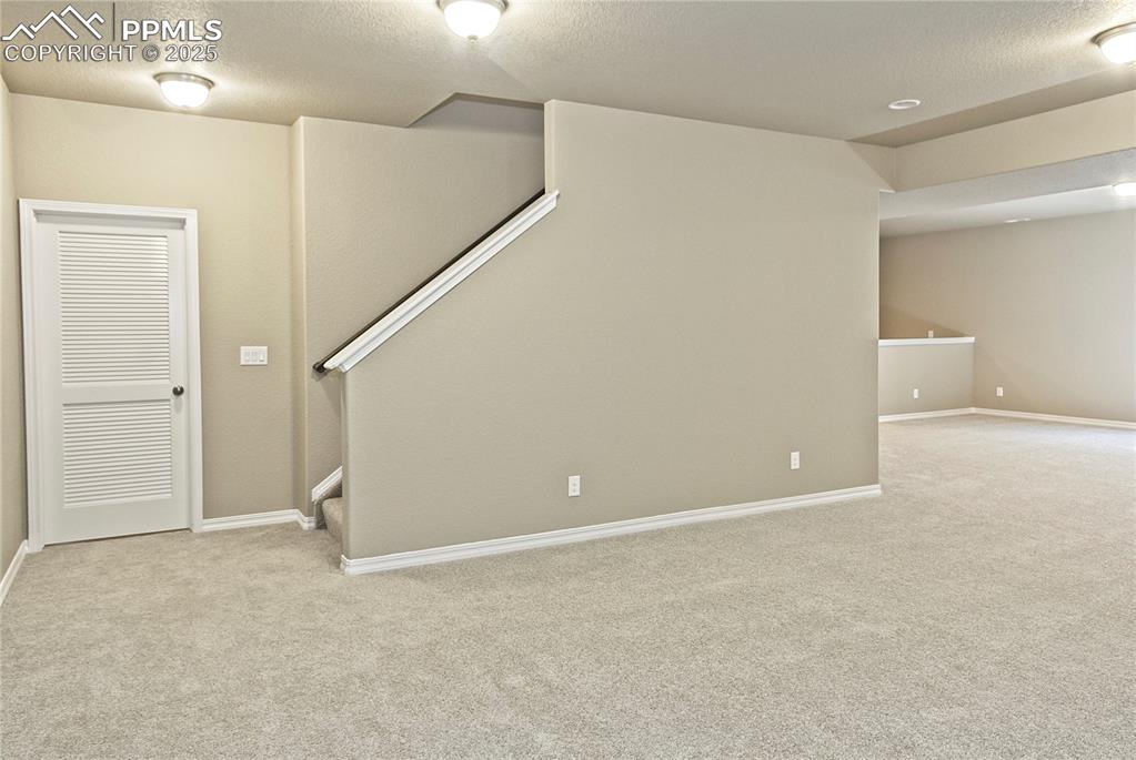 Image 19 of 25: Basement with light colored carpet, a textured ceiling, and stairway