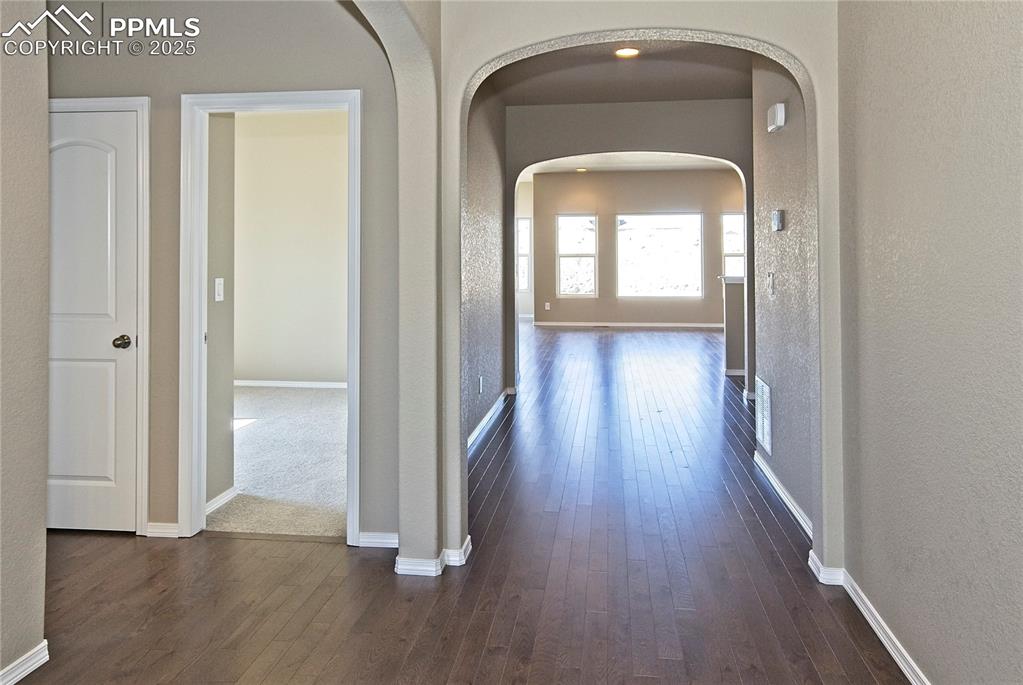 Image 2 of 25: Hall featuring arched walkways, dark wood-style floors, and a textured wall