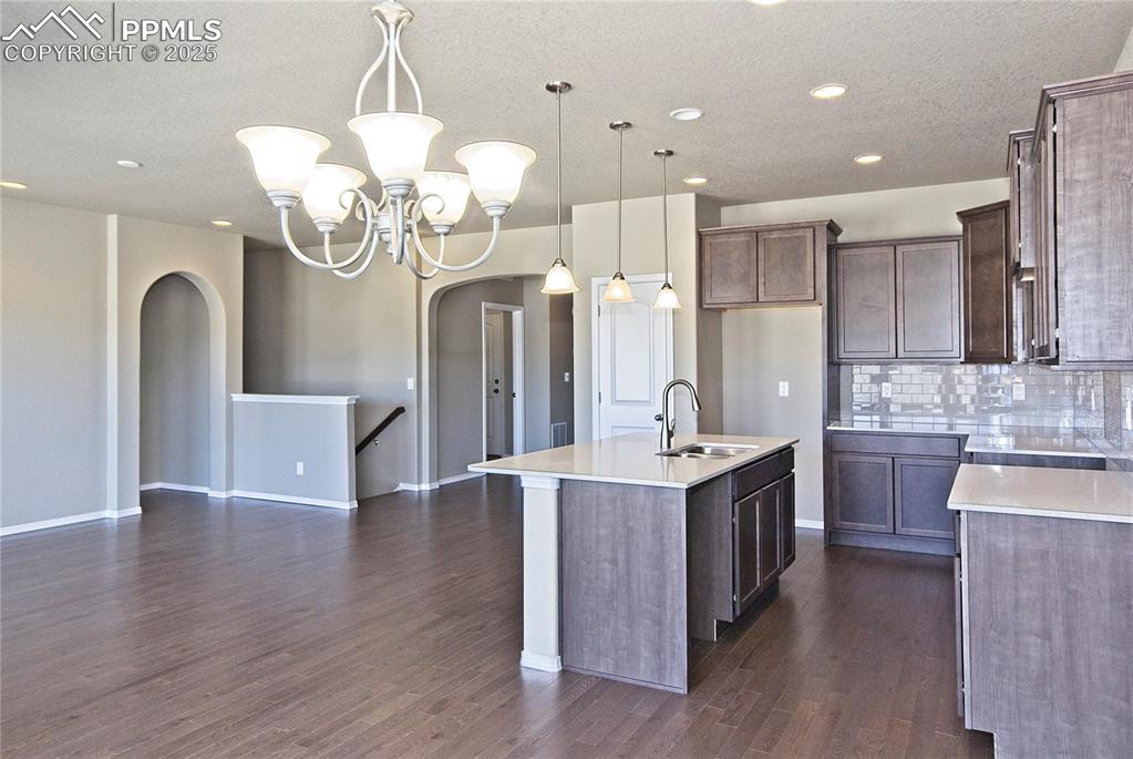 Image 5 of 25: Kitchen with arched walkways, an island with sink, backsplash, light counte