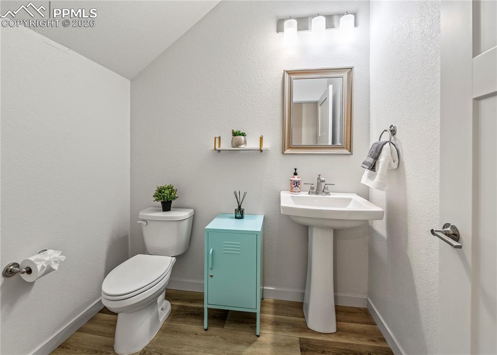 Image 21 of 46: Half bathroom featuring vaulted ceiling, light wood-type flooring, and a te