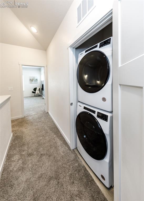 Image 40 of 46: Laundry area featuring lofted ceiling, light colored carpet, and stacked wa