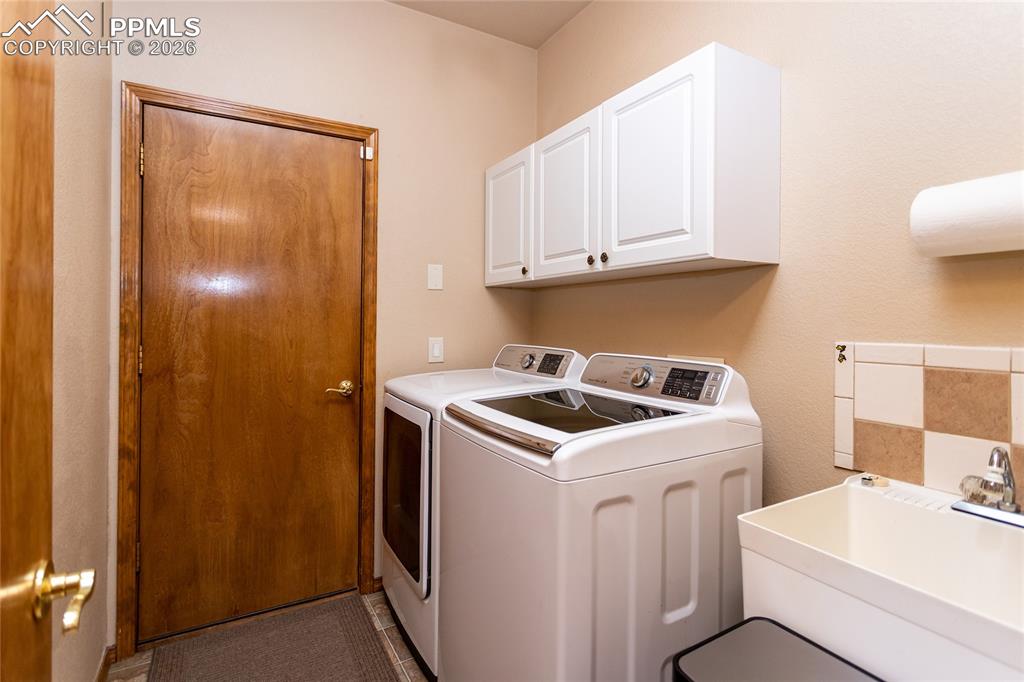 Image 21 of 50: Laundry room features a large utility sink and storage cabinets.
