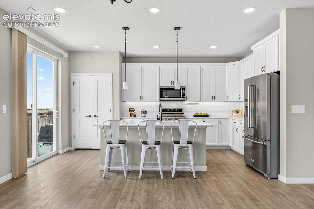 Image 23 of 47: Kitchen featuring wood-finish flooring, white cabinetry with dark hardware,