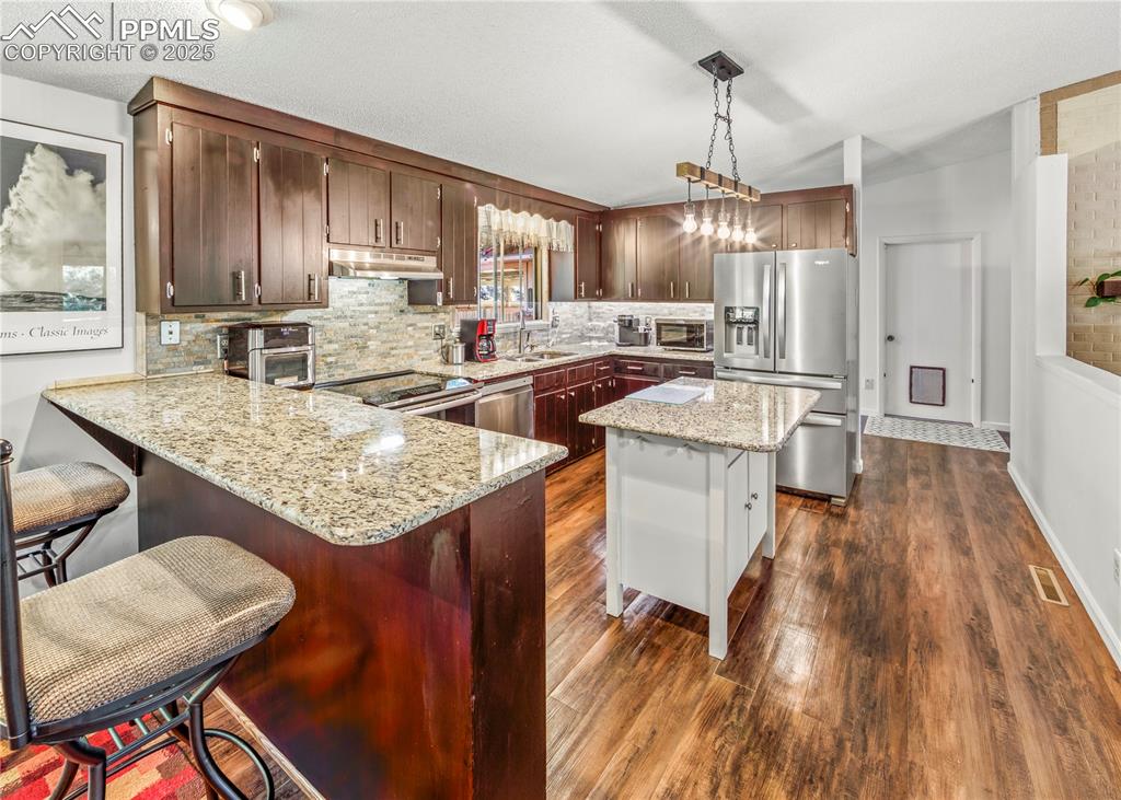 Image 5 of 33: Kitchen featuring a breakfast bar, light stone counters, stainless steel ap