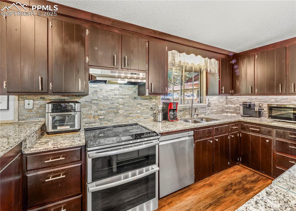 Image 6 of 33: Kitchen featuring stainless steel appliances, dark wood-type flooring, unde