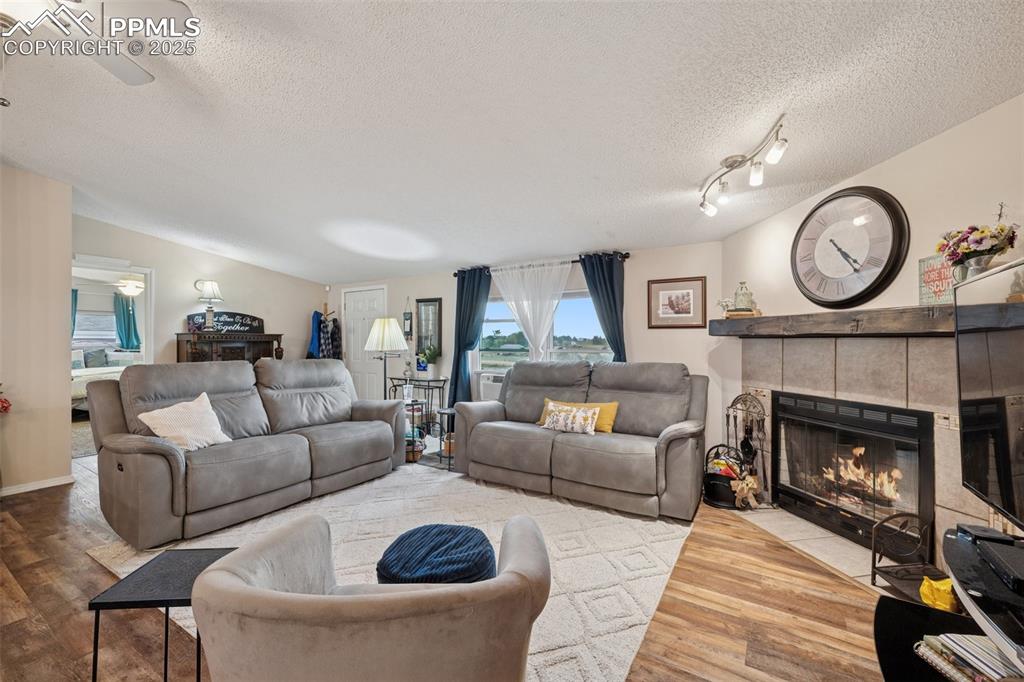 Image 14 of 33: Living room featuring a textured ceiling, LVT floors, a tiled fireplace, an