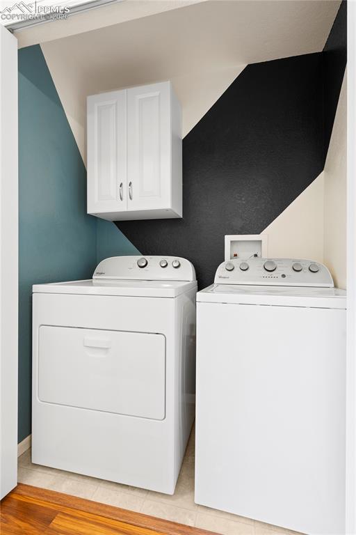 Image 19 of 27: Laundry room with washer and clothes dryer, cabinet space, and light wood f