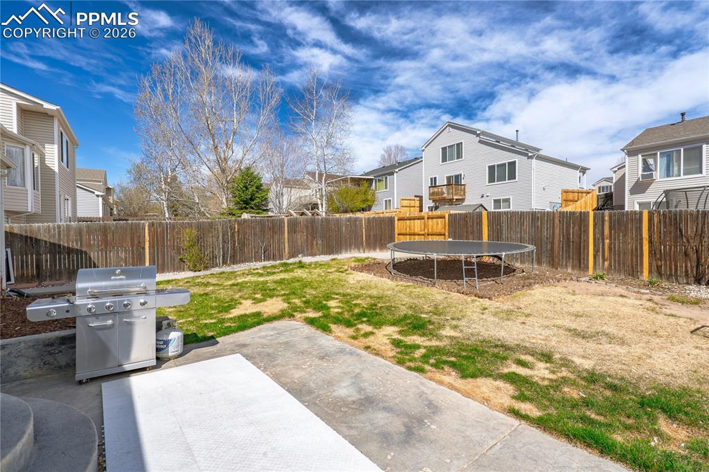 Image 5 of 27: Fenced backyard featuring a trampoline, a patio area, and a residential vie