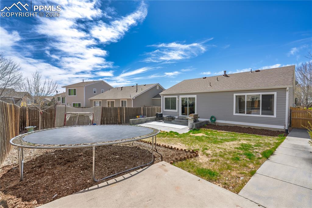 Image 6 of 27: Back of house featuring a fenced backyard, a patio area, and a trampoline