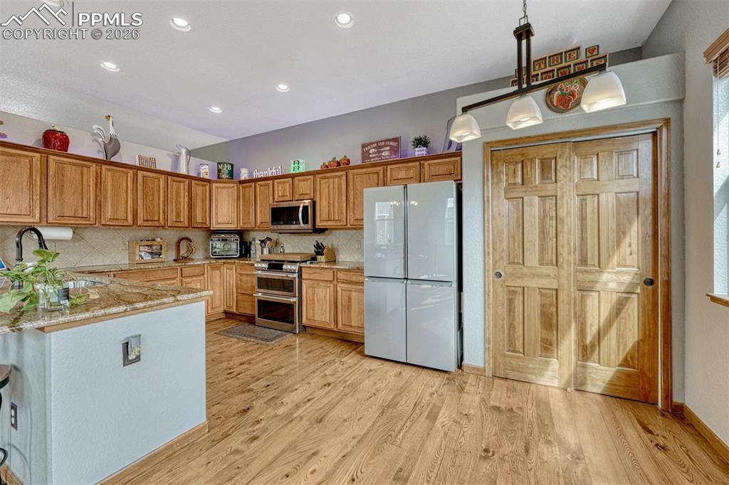 Image 13 of 45: Kitchen with stainless steel appliances, light stone counters, light wood f