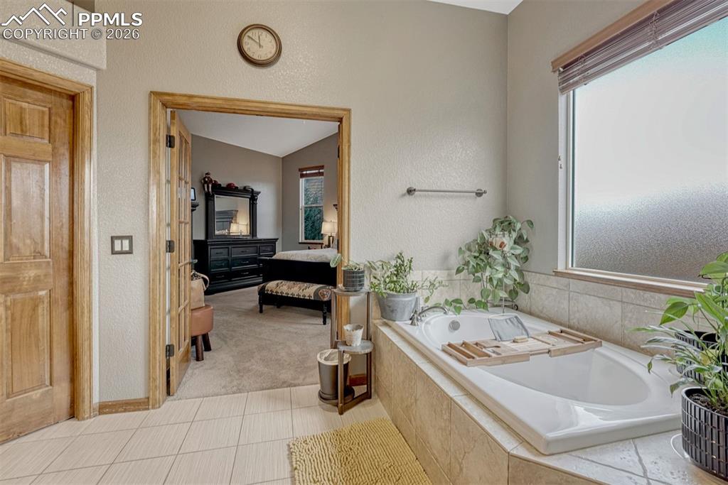 Image 16 of 45: Primary bathroom. Bathtub, vaulted ceiling, light tile floors, Shower