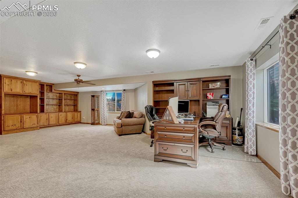 Image 26 of 45: Office set up in the basement with ceiling fan, light carpet, and a texture