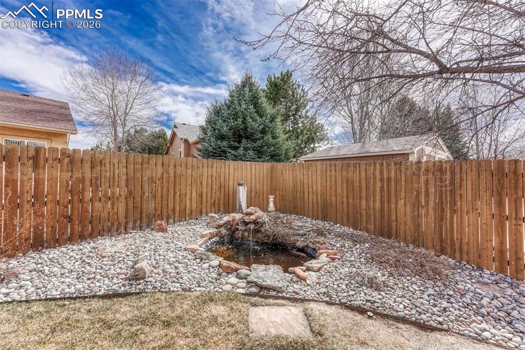 Image 37 of 45: Fenced backyard featuring a garden pond. Beautiful flowers bloom in the spr