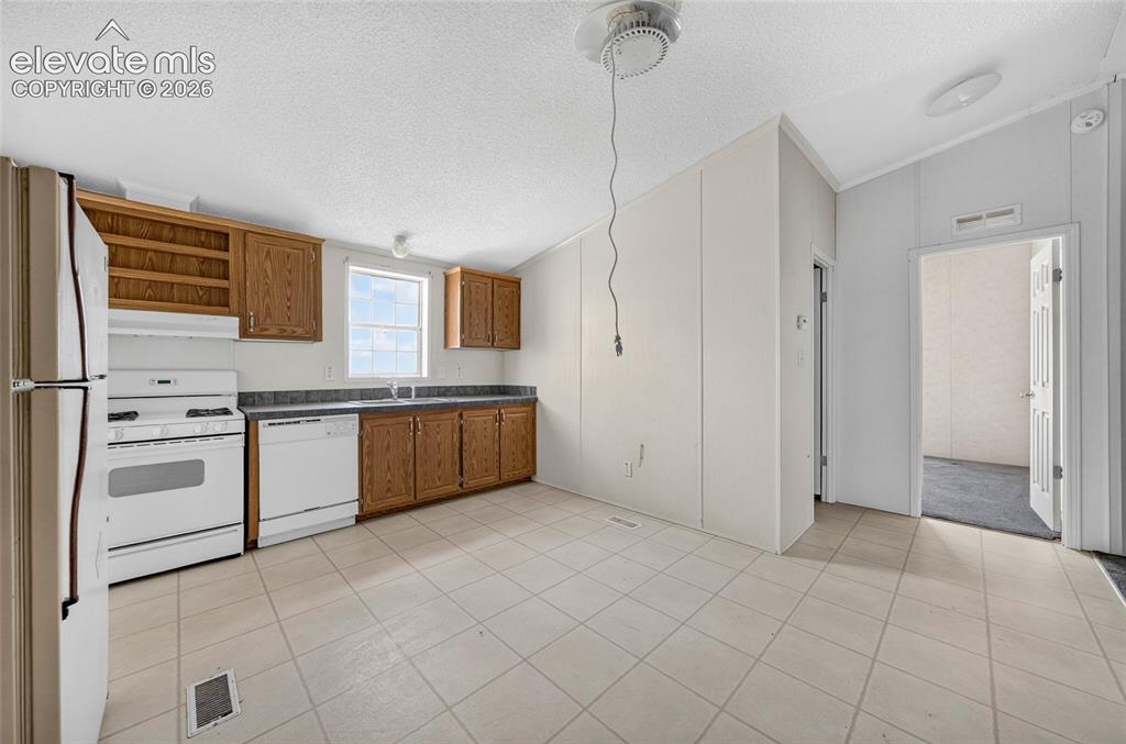 Image 9 of 41: Kitchen featuring wood cabinetry, white appliances, dark countertops, a win