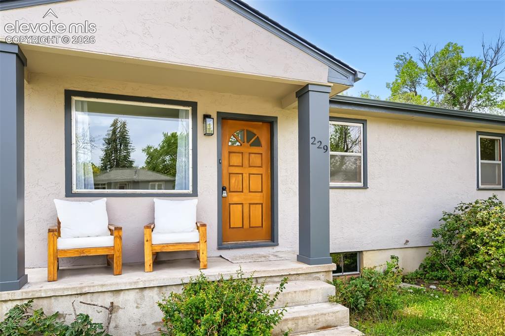 Caption: Front exterior with textured stucco finish, dark trim windows, and a wood-panel entry door with tran