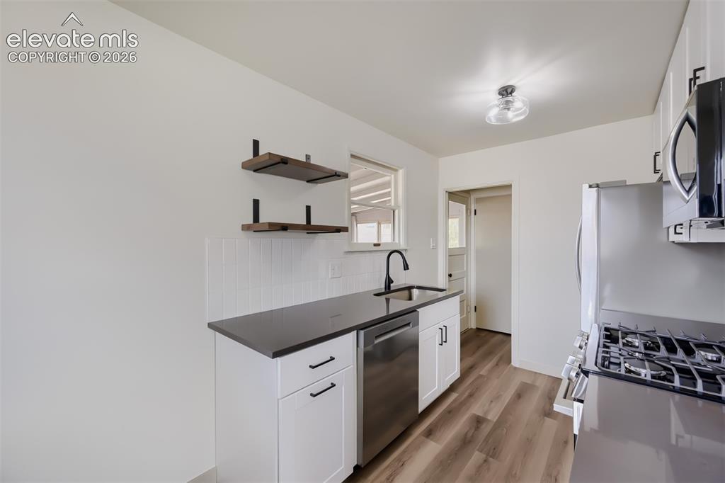 Image 11 of 41: Contemporary kitchen featuring white cabinetry, dark countertops, stainless