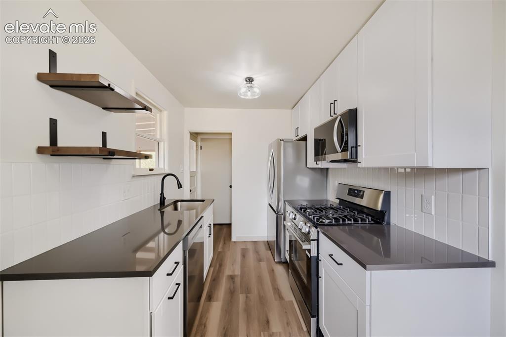 Image 12 of 41: Modern kitchen featuring white cabinetry, dark countertops, wood-finish flo