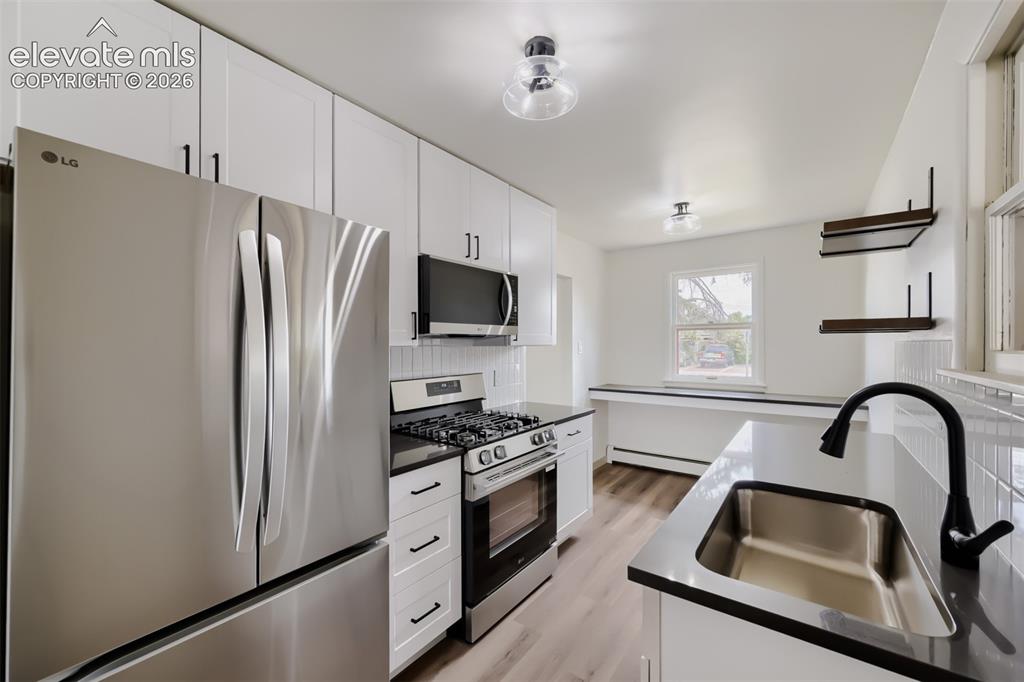Image 13 of 41: Stainless steel appliances, white shaker cabinetry, dark countertops, a sta