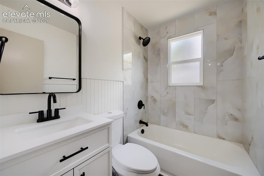 Image 21 of 41: White vanity with solid surface countertop, matte black fixtures, full tile