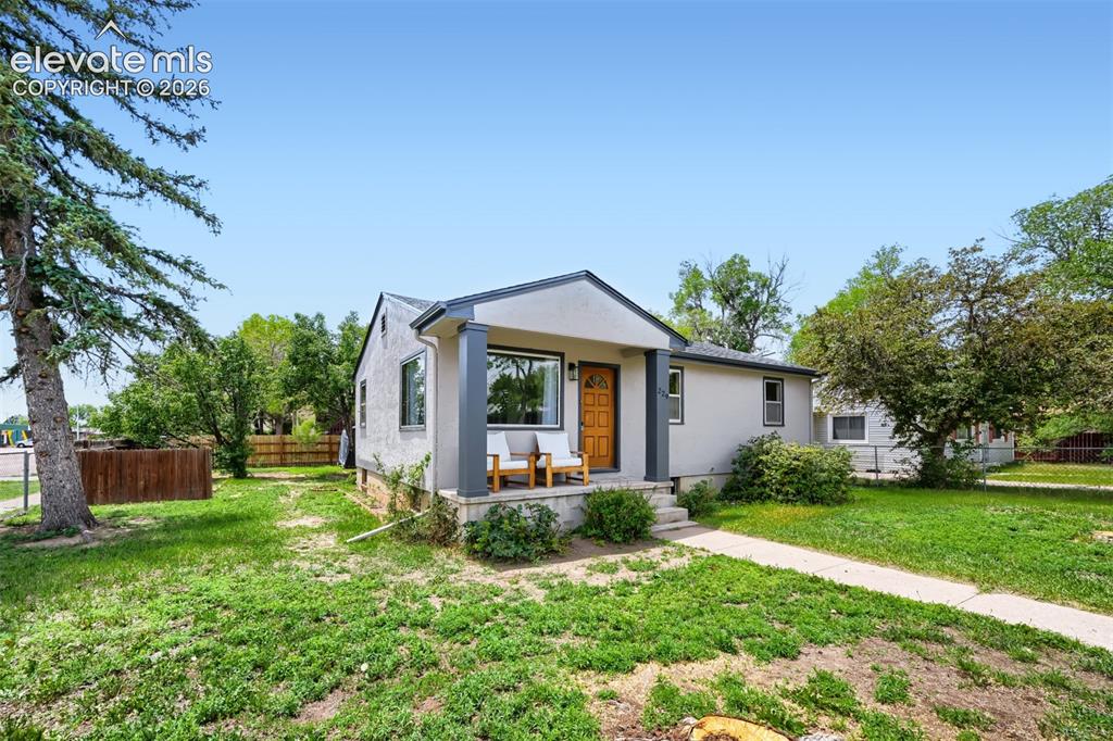 Image 37 of 41: Stucco exterior with a covered front porch, wood-finish front door, and est