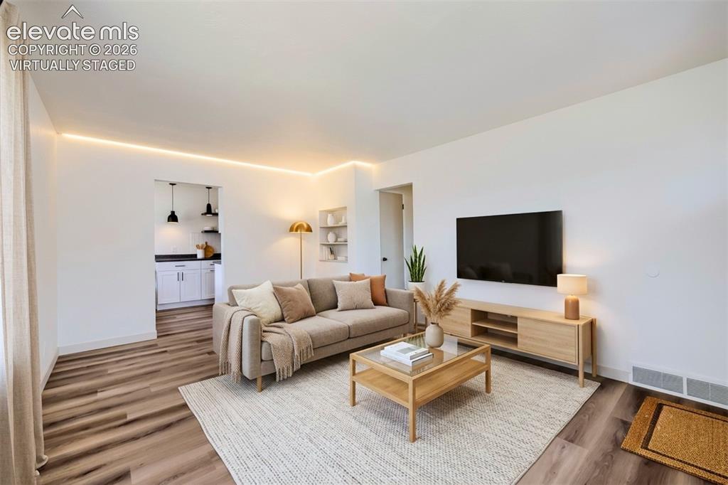Image 7 of 41: Bright living space featuring wood-finish flooring and integrated cove ligh