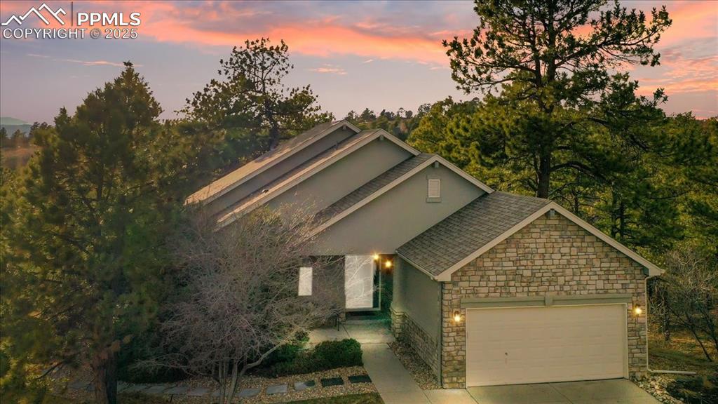 Caption: View of front facade featuring stone siding, a garage, stucco siding, driveway, and a shingled roof