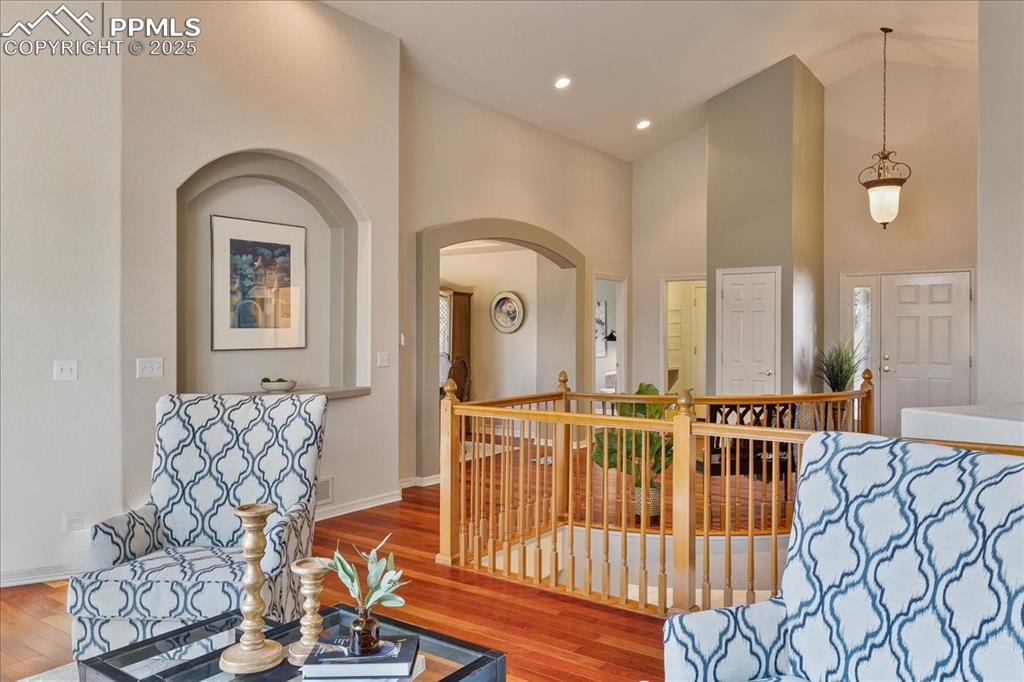 Image 4 of 46: Sitting room with wood finished floors, high vaulted ceiling, arched walkwa