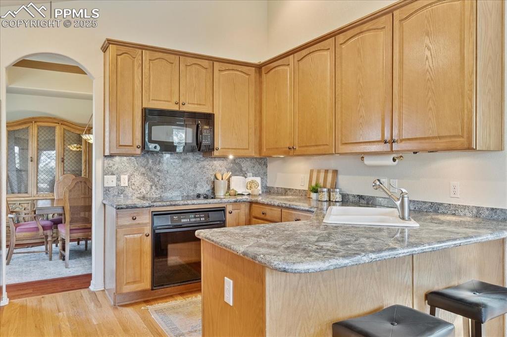 Image 7 of 46: Kitchen featuring black appliances, a peninsula, a breakfast bar, arched wa
