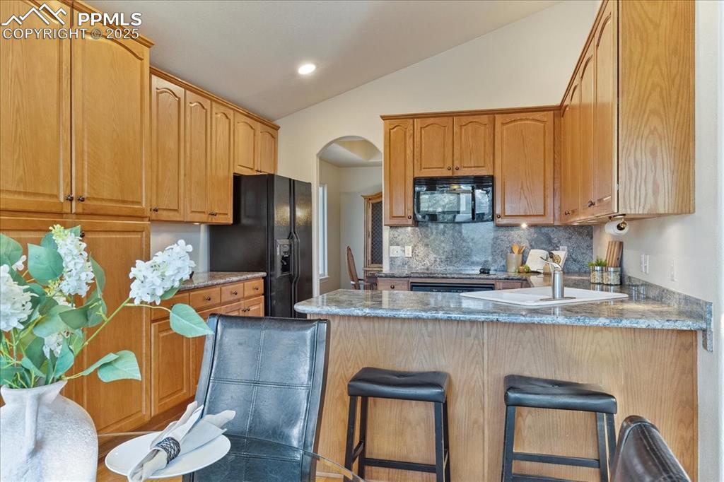 Image 8 of 46: Kitchen with a peninsula, black appliances, lofted ceiling, a breakfast bar