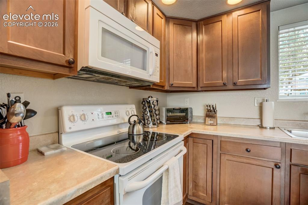 Image 14 of 50: Wood-finish cabinetry, solid surface countertops, white electric range, ove