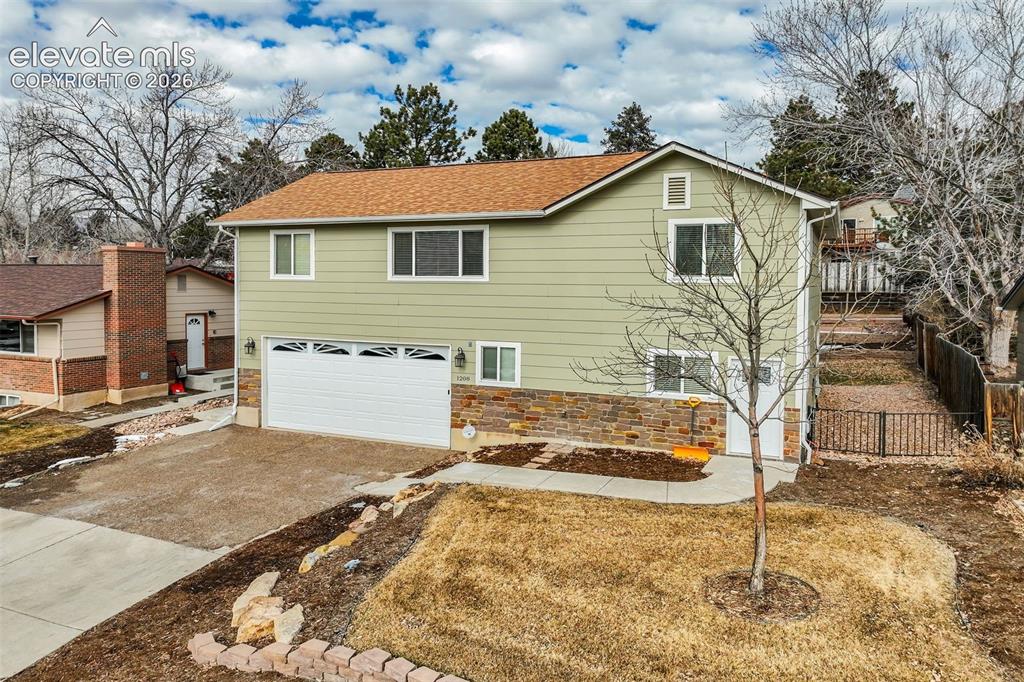 Image 2 of 50: Light green siding exterior with a stone-finish foundation, two-car garage,