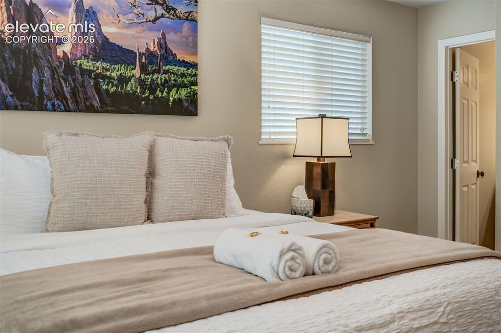 Image 25 of 50: Window with horizontal blinds and a nightstand featuring a table lamp
