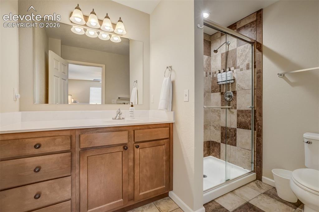 Image 28 of 50: Vanity with wood-finish cabinetry, white countertop, and a wide mirror