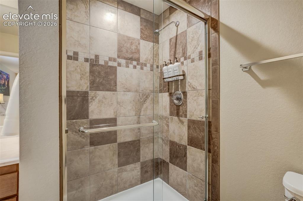 Image 29 of 50: Glass-enclosed shower with a tiled surround, featuring a decorative tile ba