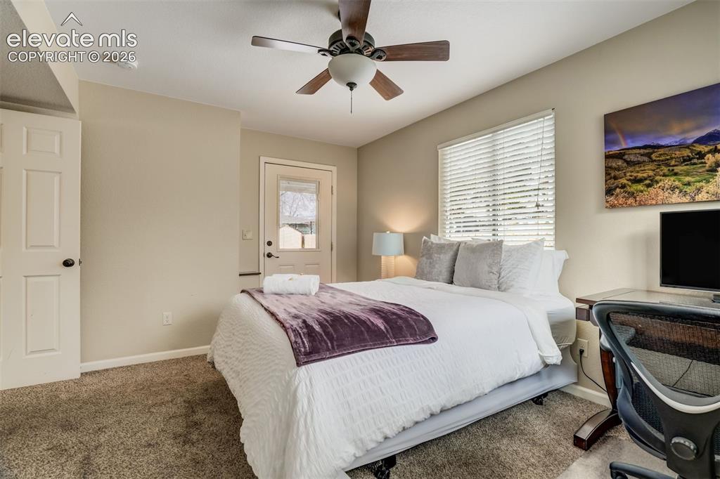 Image 40 of 50: Carpeted room with a ceiling fan, window with blinds, and white door