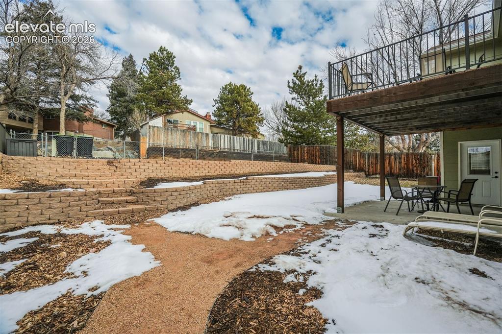 Image 43 of 50: Tiered retaining walls, paved patio, upper-level deck with metal railing, a