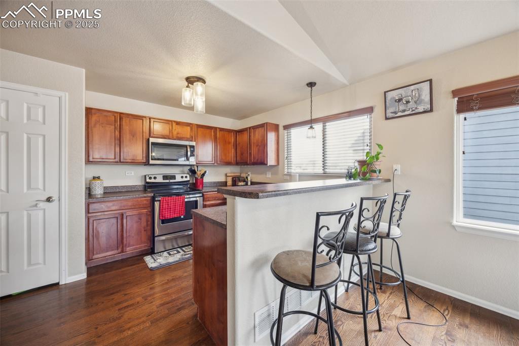 Image 7 of 29: Kitchen featuring dark wood-type flooring, a peninsula, a breakfast bar, ap