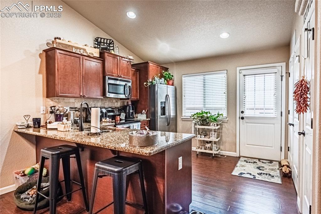 Image 10 of 36: Kitchen featuring a textured wall, a peninsula, light stone counters, stain