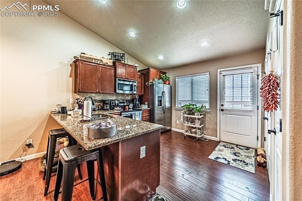 Image 11 of 36: Kitchen with dark stone counters, vaulted ceiling, a peninsula, a breakfast