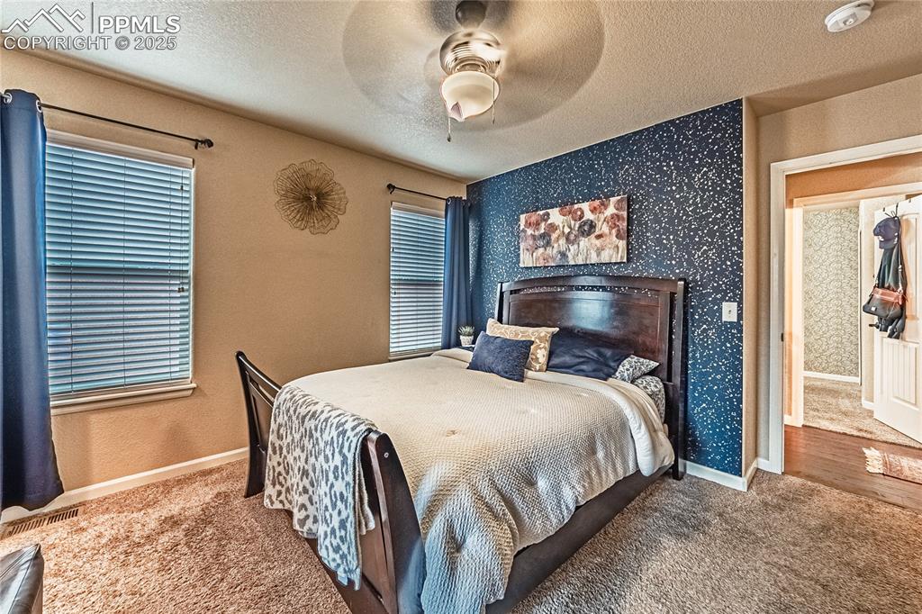 Image 14 of 36: Carpeted bedroom with a textured ceiling, a ceiling fan, and wallpapered wa