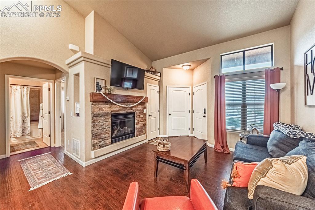 Image 3 of 36: Living room with arched walkways, dark wood-style floors, a stone fireplace