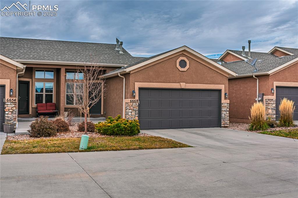 Image 35 of 36: Ranch-style home with stone siding, stucco siding, a garage, and concrete d
