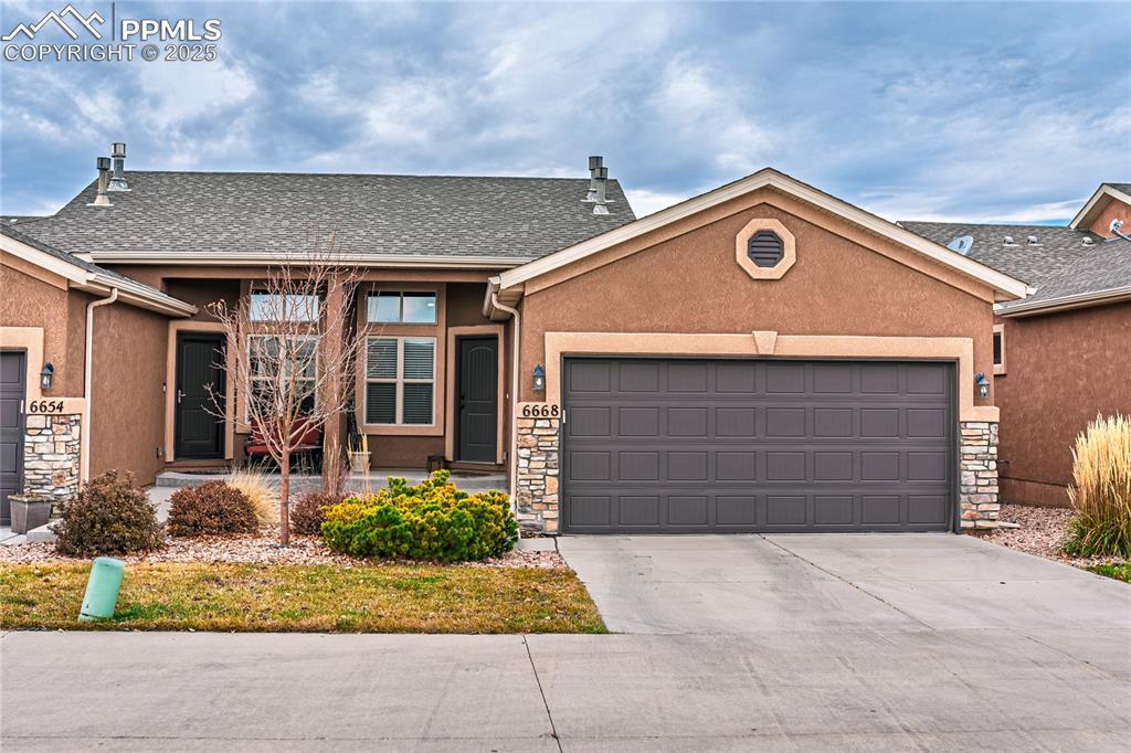 Image 36 of 36: Single story home with a garage, stone siding, stucco siding, and driveway