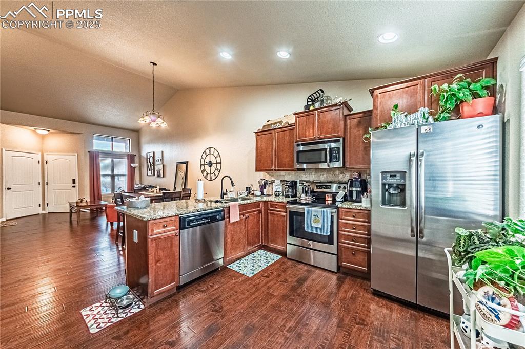Image 8 of 36: Kitchen with stainless steel appliances, lofted ceiling, light stone counte