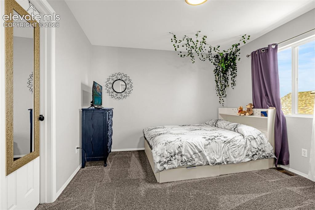 Image 19 of 42: Carpeted room with light grey walls, a single window with purple drapes, an