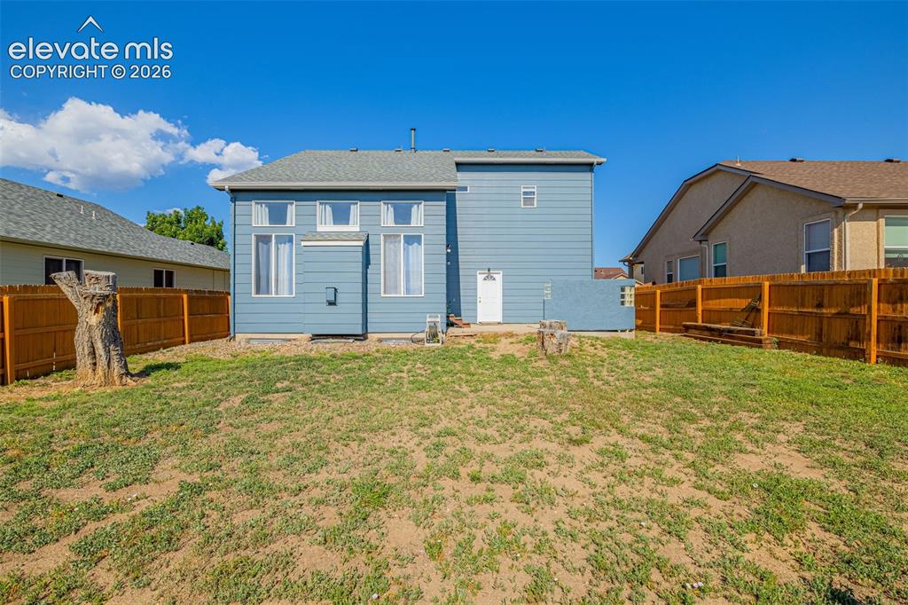 Image 27 of 42: Expansive backyard with a manicured lawn, full wood fencing, and visible ex