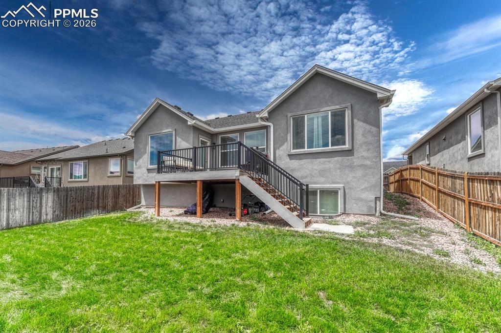 Image 8 of 50: Rear view of home and fenced backyard with composite deck and stairs to the