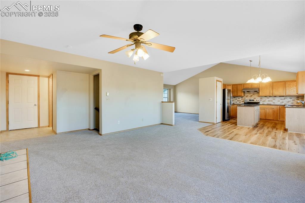 Image 10 of 32: Unfurnished living room with light carpet, lofted ceiling, a chandelier, an