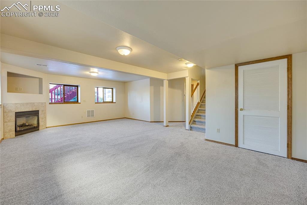 Image 21 of 32: Unfurnished living room with stairway, carpet, and a tiled fireplace